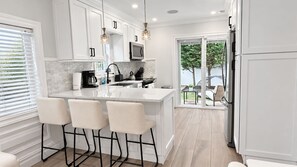 A modern kitchen with white cabinetry, a central island with bar stools, a microwave, and a refrigerator.