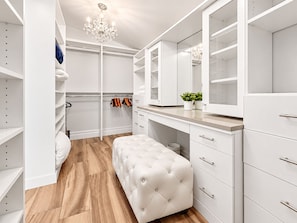 A walk-in closet with white shelving, a mirrored vanity, and a tufted bench.