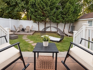 A backyard patio with a table, chairs, a swing, and a potted plant.