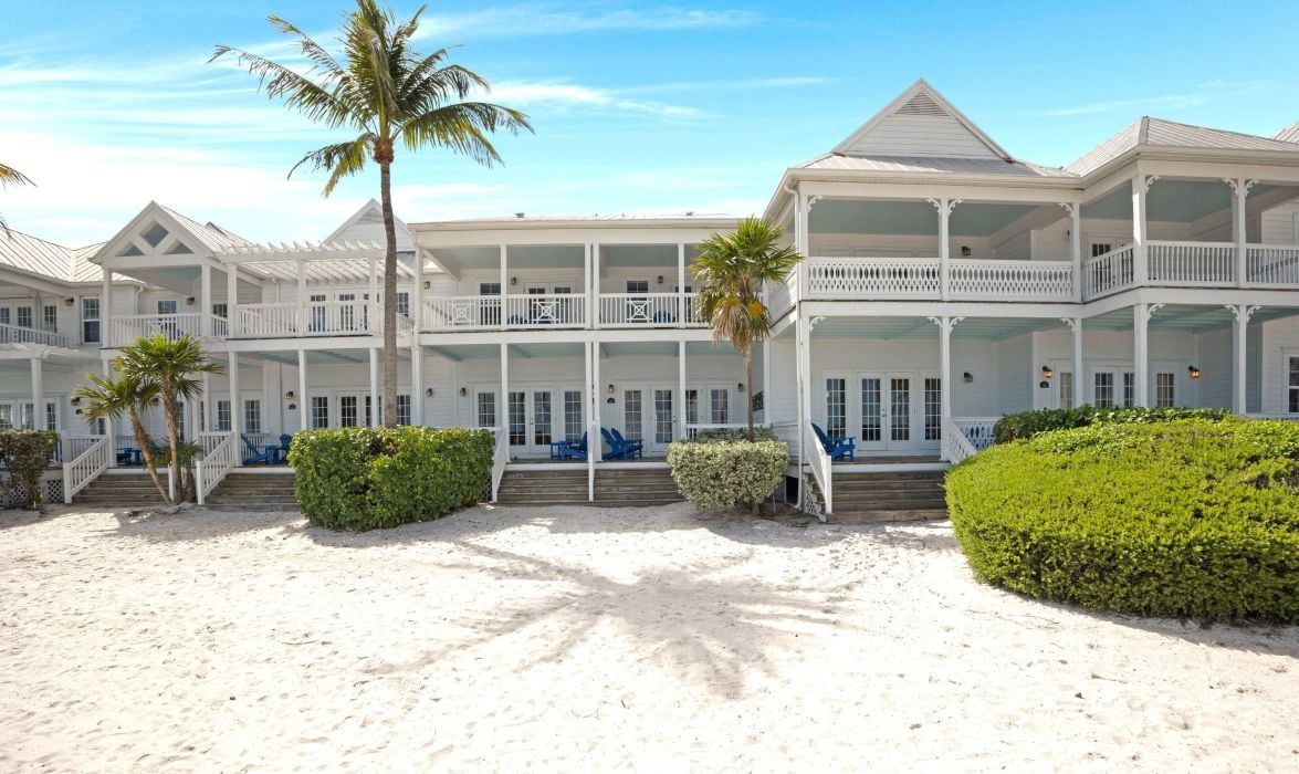 A beachfront hotel with multiple balconies, a sandy beach, and palm trees.
