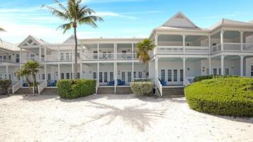 A beachfront hotel with multiple balconies, a sandy beach, and palm trees.