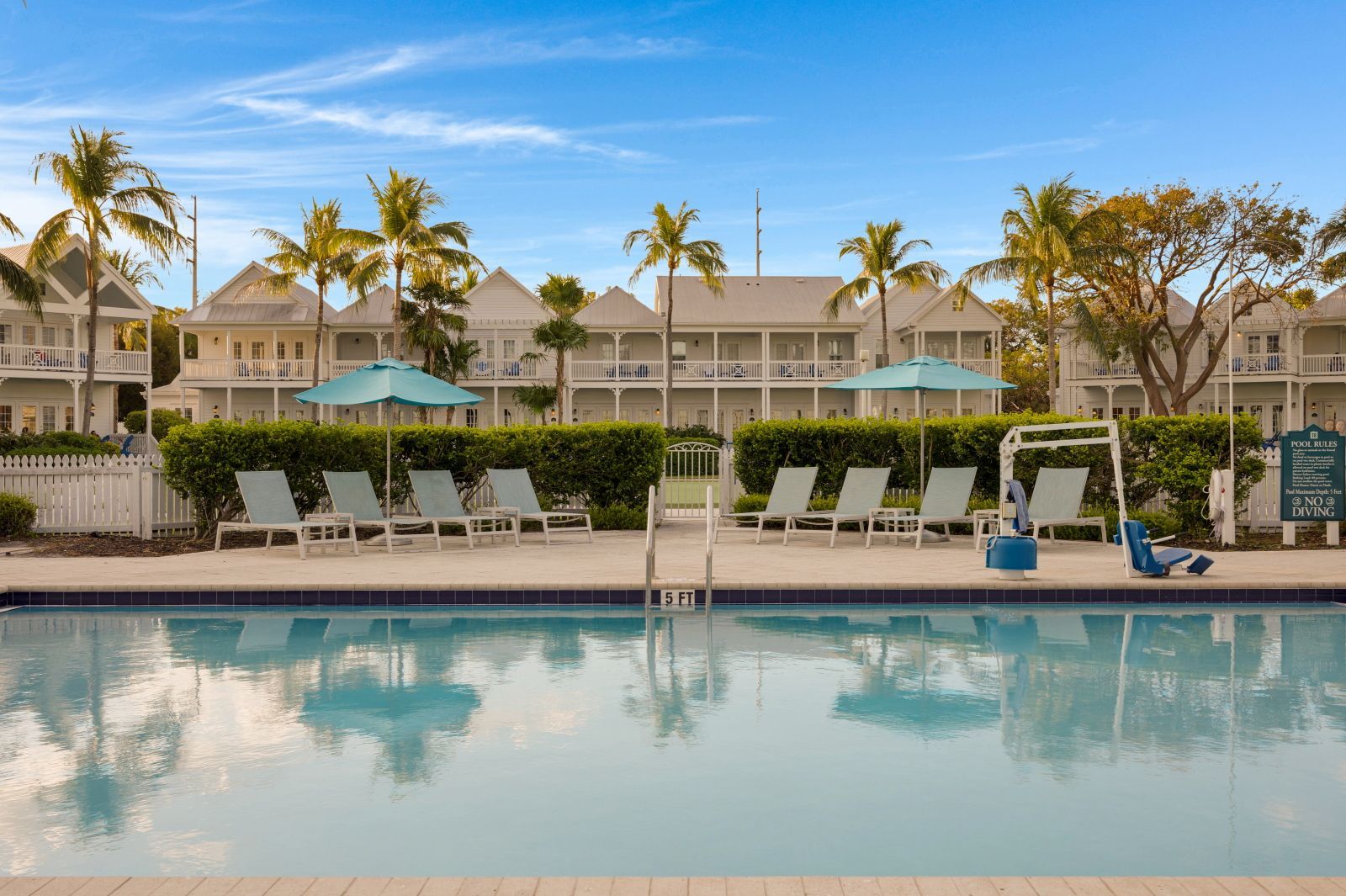 A pool area with lounge chairs and umbrellas, a pool with a 5 FT depth marker, and a sign indicating pool rules.