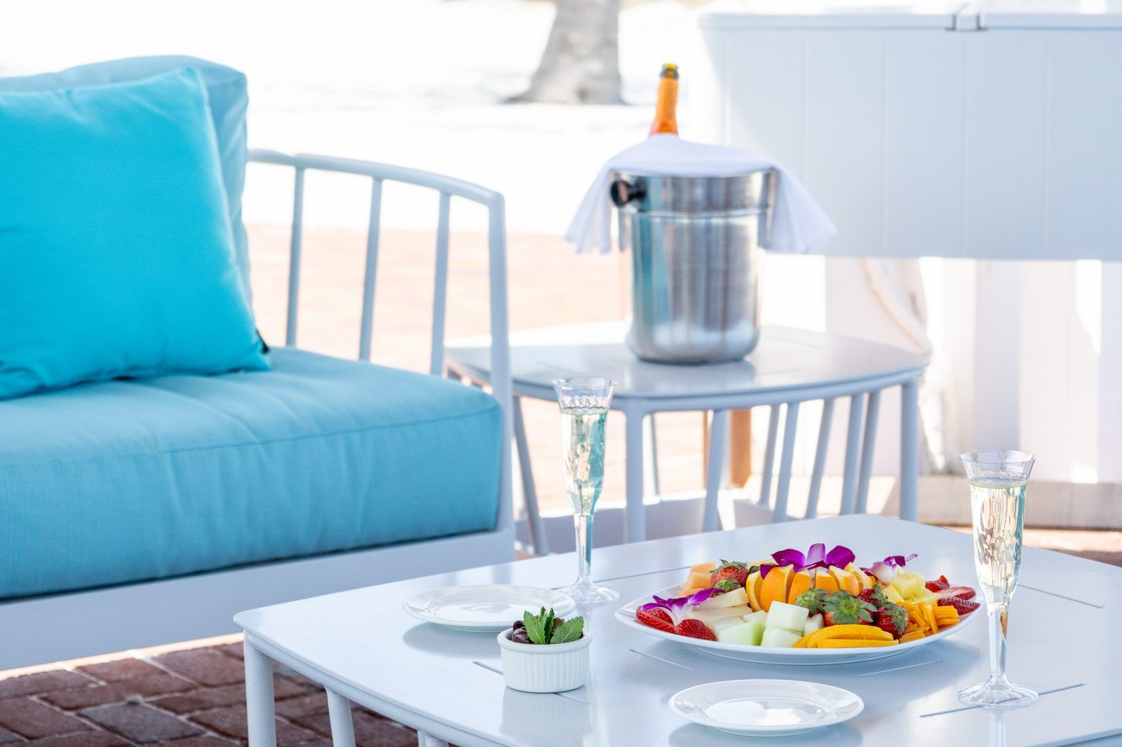 Une table sur laquelle se trouve une assiette de fruits, deux coupes de champagne et une bouteille de champagne, le tout posé sur une table blanche.