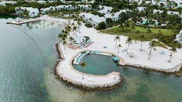 An aerial view of a resort with a circular water feature, surrounded by palm trees and a dock with boats.