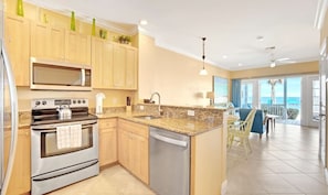 A modern kitchen with stainless steel appliances, a granite countertop, and a view of the ocean through large windows.