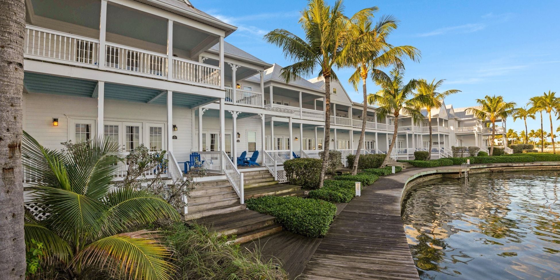 A waterfront hotel with multiple balconies, a wooden deck, and palm trees.