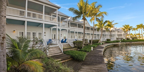 A waterfront hotel with multiple balconies, a wooden deck, and palm trees.