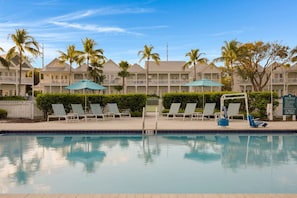 A pool area with lounge chairs and umbrellas, a sign indicating pool rules, and a building with balconies and palm trees in the background. - Waterfront Villa w/ Uninterrupted Ocean Views (Marathon)