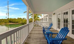 A wooden deck with blue chairs, a white railing, and a view of the water.