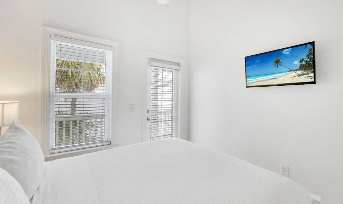 A bedroom with a bed, two windows with blinds, and a TV on the wall.