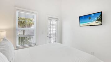 A bedroom with a bed, two windows with blinds, and a TV on the wall.