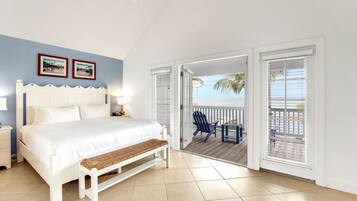 A bedroom with a bed, bedside table, bench, and a view of a balcony with chairs.