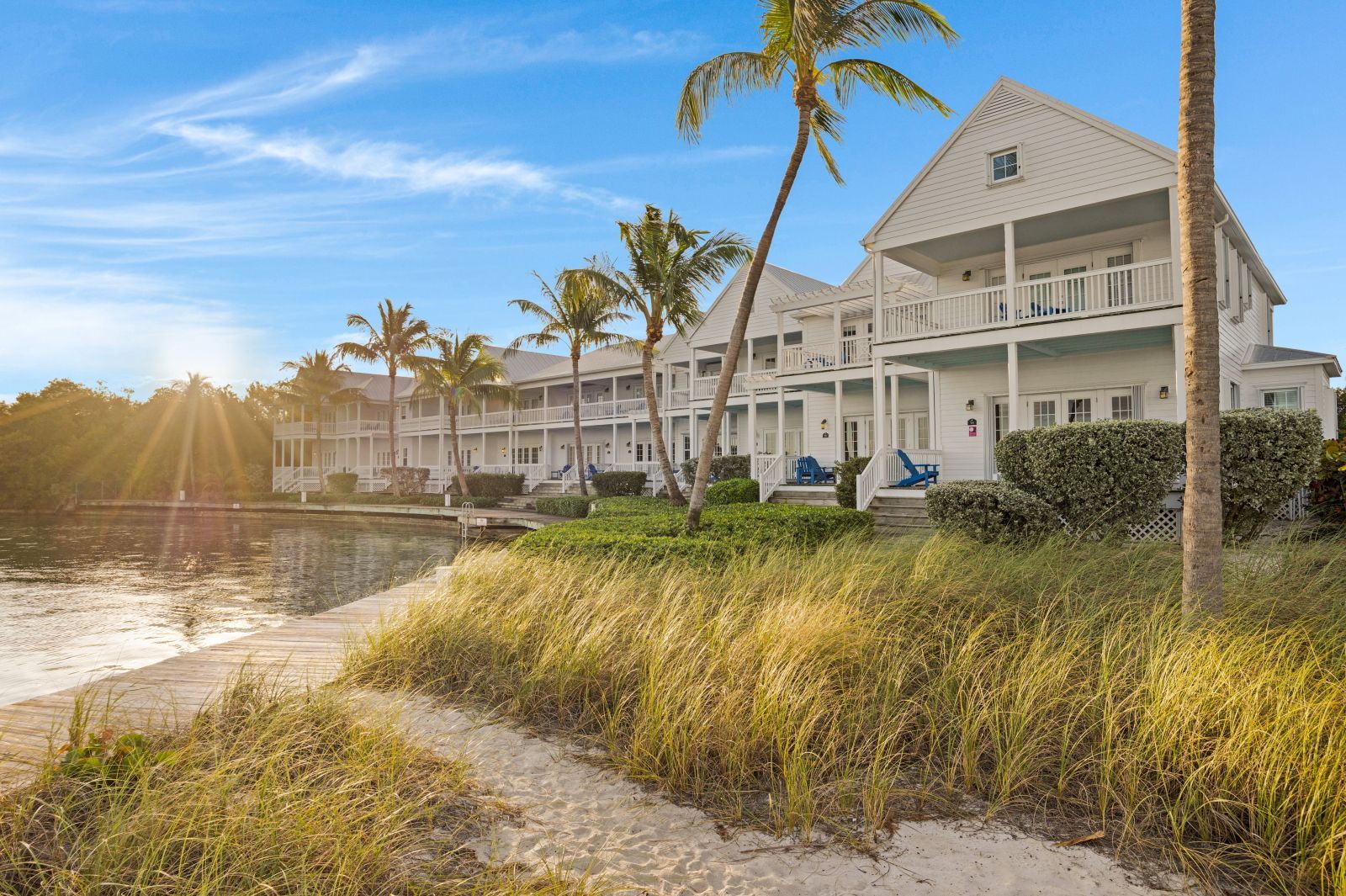 Un hôtel situé en bord de mer, doté de nombreux balcons, d’un quai et de palmiers.