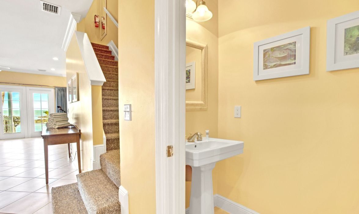A hallway with a staircase, a white sink, and framed artwork on the walls.