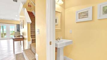 A hallway with a staircase, a white sink, and framed artwork on the walls.