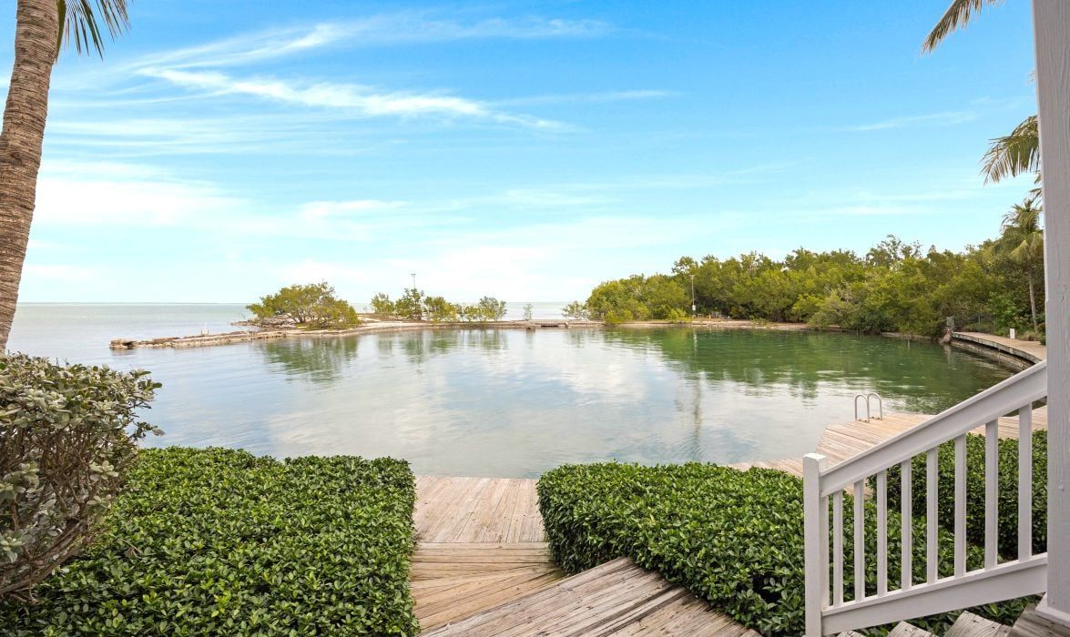 A wooden deck leading to a calm water body with a clear sky above.