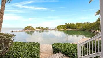 A wooden deck leading to a calm water body with a clear sky above.