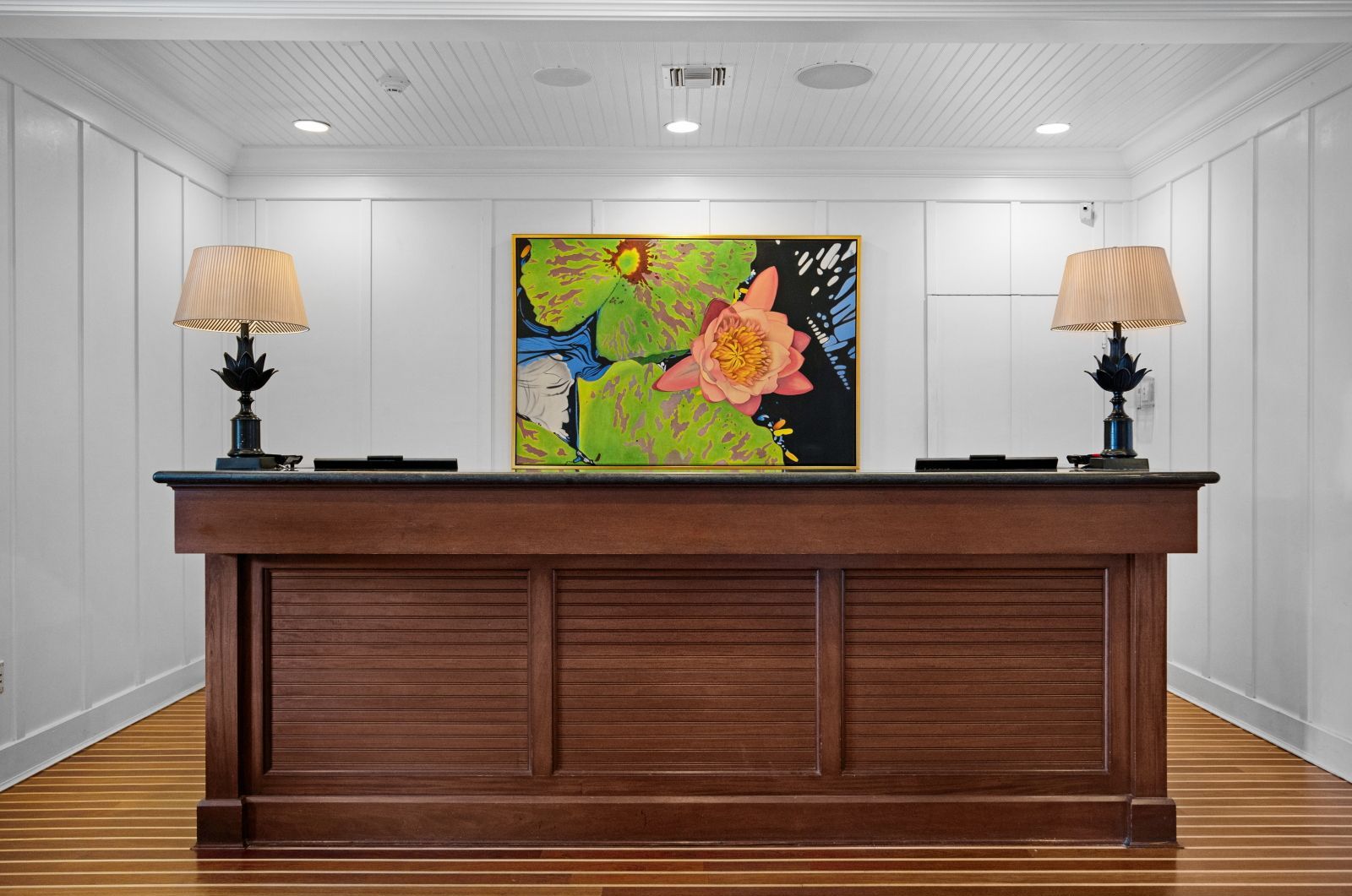 Wooden reception desk with lamps and a floral painting on the wall behind.