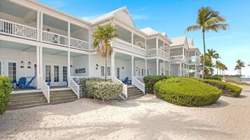 A beachfront hotel with multiple balconies, a sandy walkway, and palm trees.