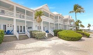 A beachfront hotel with multiple balconies, a sandy walkway, and palm trees.