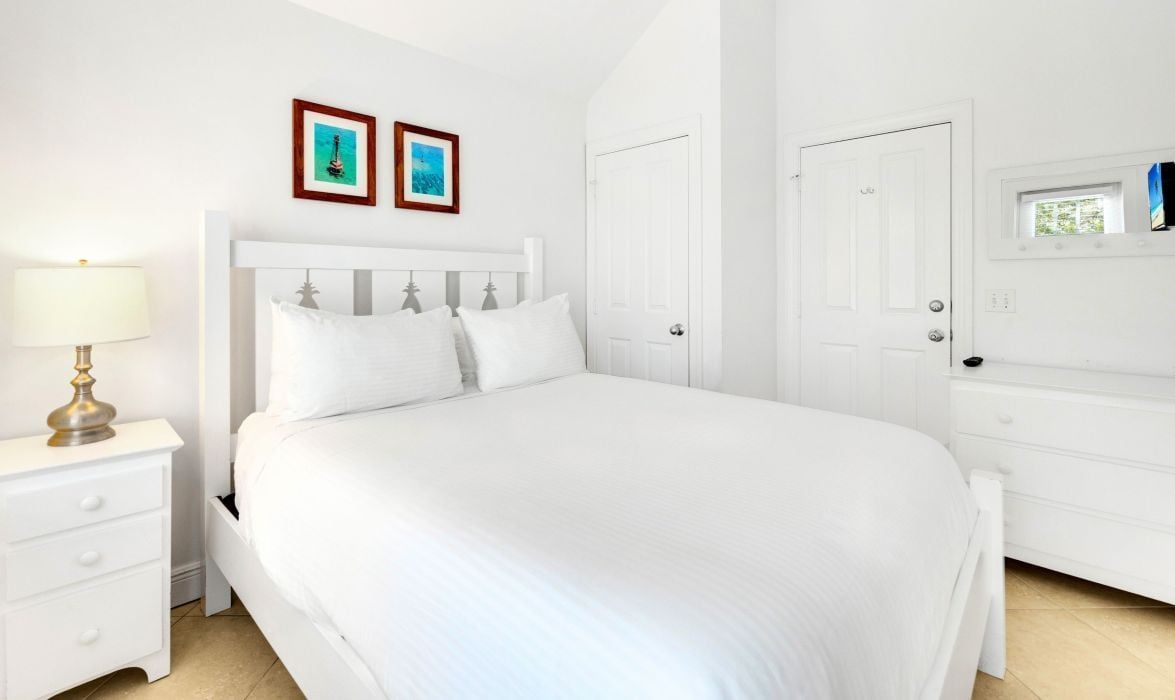 A white bedroom with a bed, a nightstand, a dresser, and two framed pictures on the wall.