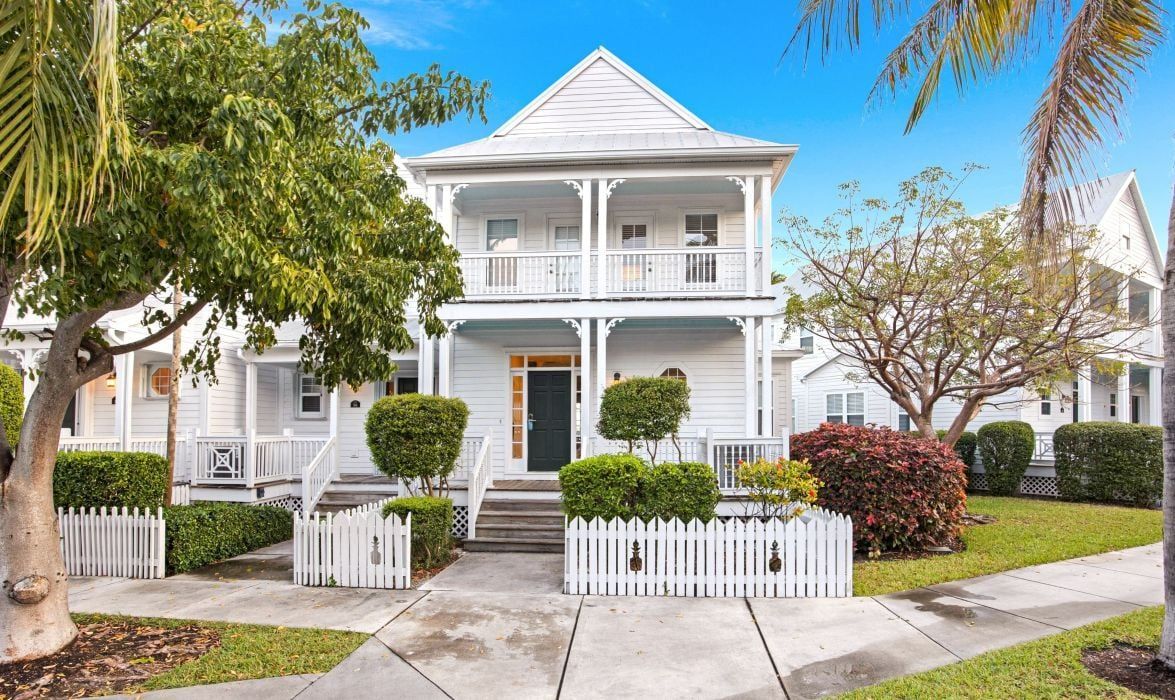 A two-story white house with a front porch, a picket fence, and a well-maintained lawn.