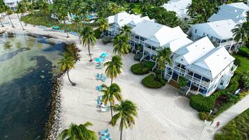 A resort with multiple white buildings, a sandy beach, and palm trees.