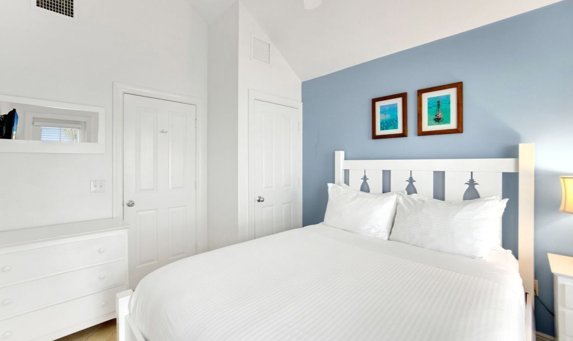 A bedroom with a white bed, a white dresser, and a blue accent wall.