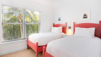 Une chambre avec deux lits, une fenêtre avec des stores et deux tables de chevet fixées au mur.