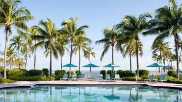 A pool area with palm trees, lounge chairs, and umbrellas.