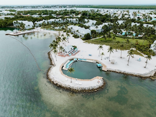 An aerial view of a resort with a circular water feature, surrounded by palm trees and a dock with boats.