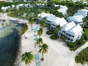 A resort with multiple white buildings, a sandy beach, and palm trees.