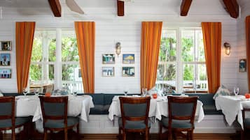 Dining area at Butterfly Cafe with orange curtains, white table settings, and a window-side bench.