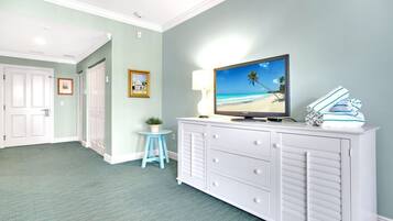 A room with a television on a white dresser, a small blue stool, and a framed picture on the wall.