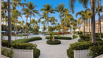 A resort with a central pool, surrounded by palm trees and a white picket fence.