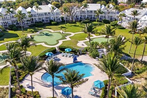 A resort with a swimming pool, lounge chairs, and palm trees.
