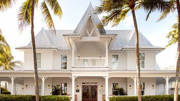 A white colonial-style building with a central entrance, flanked by two palm trees and a manicured hedge.