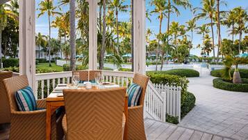 A covered outdoor seating area with wicker furniture and a view of palm trees.