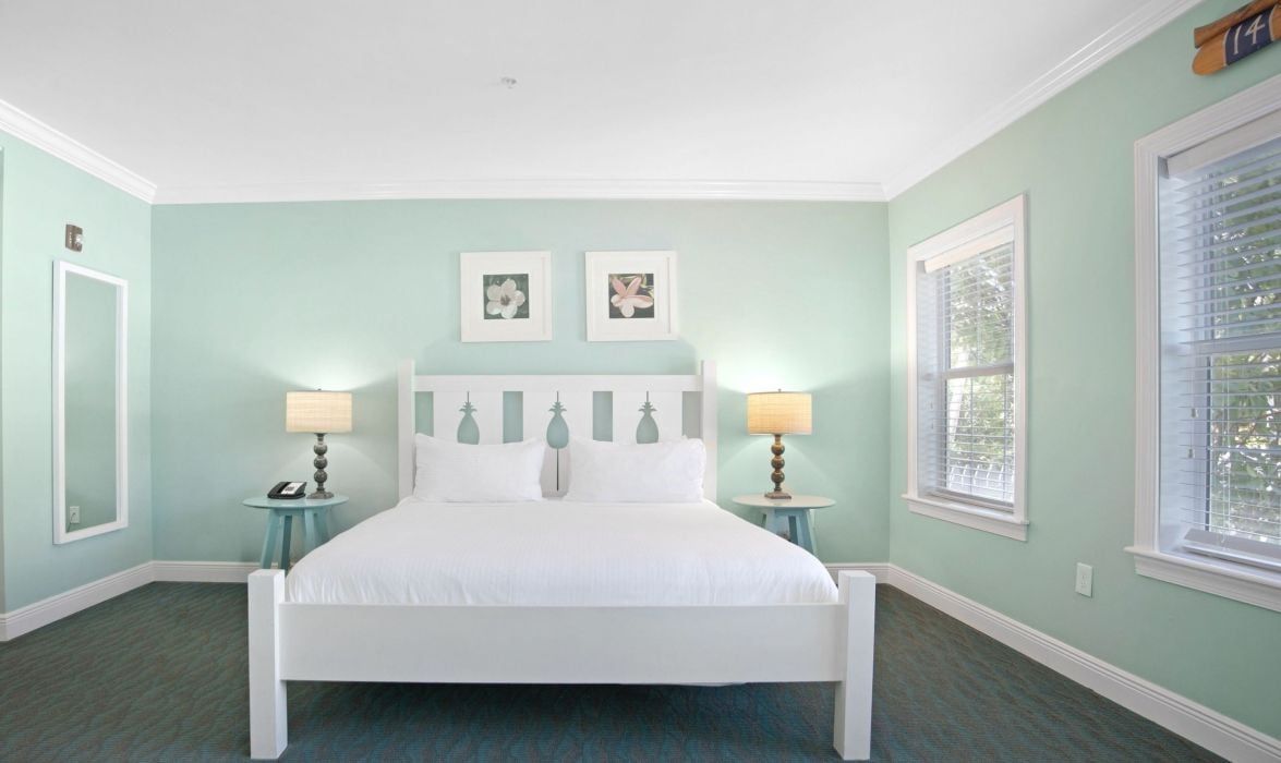 A bedroom with a white bed, two bedside tables with lamps, a headboard with a tree design, and two framed pictures on the wall.