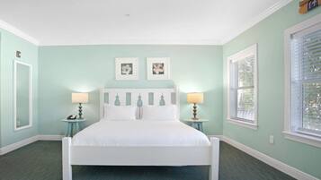 A bedroom with a white bed, two bedside tables with lamps, a headboard with a tree design, and two framed pictures on the wall.