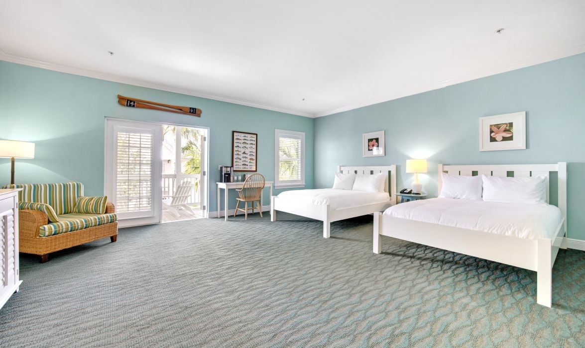 A bedroom with two beds, a chair, a desk, and a window.