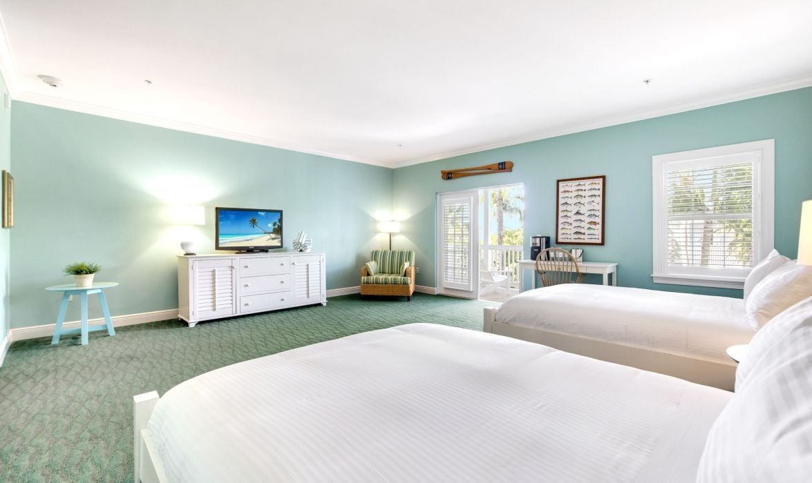 A bedroom with two beds, a dresser, a television, and a window with blinds.