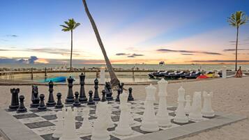 A chessboard set up on a beach with a sunset in the background.