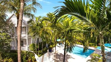 A pool area with lounge chairs and palm trees, surrounded by a white fence and a building with balconies.