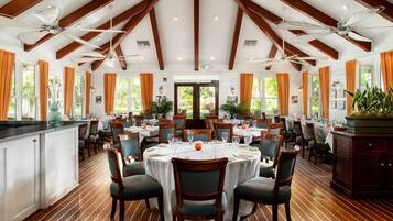 A spacious dining area with high ceilings, wooden beams, and multiple tables set for dining.