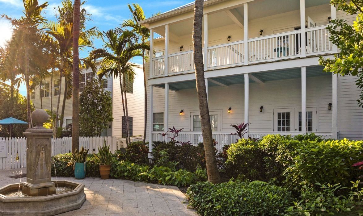 A two-story building with a balcony, surrounded by lush greenery and a fountain.