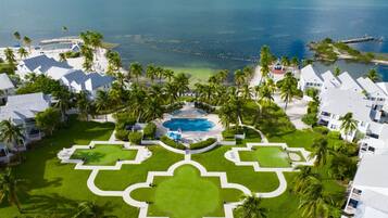 A resort with a central pool, surrounded by manicured lawns and palm trees, with a view of the ocean.