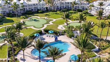 A resort with a swimming pool, lounge chairs, and palm trees.