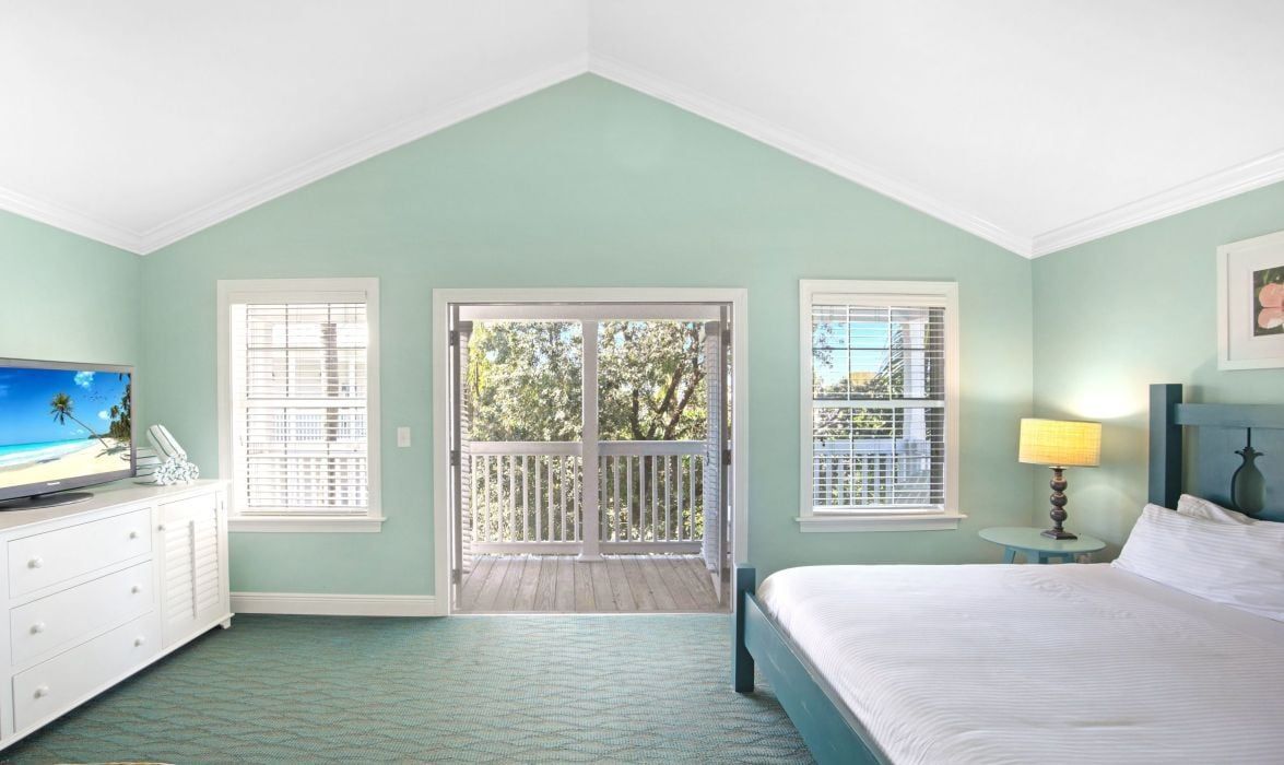 A bedroom with a bed, a dresser, a television, and a balcony with a view of trees.