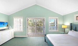 A bedroom with a bed, a dresser, a television, and a balcony with a view of trees.